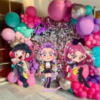 K-Pop Demon Hunter themed photo backdrop with cartoon character cut-outs, colourful balloon garland, and disco balls for a kids’ party.