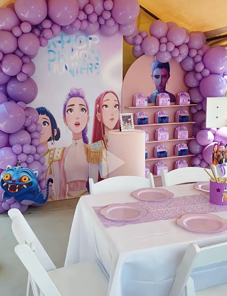 K-Pop Demon Hunter birthday party setup with purple balloon arch, themed backdrop, and pink tableware arranged for kids’ party dining.