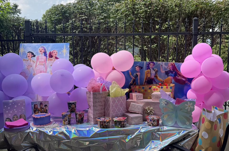 K-Pop Demon Hunter themed birthday party setup with pink and purple balloons, themed posters, and colourful presents arranged on a shimmering table.